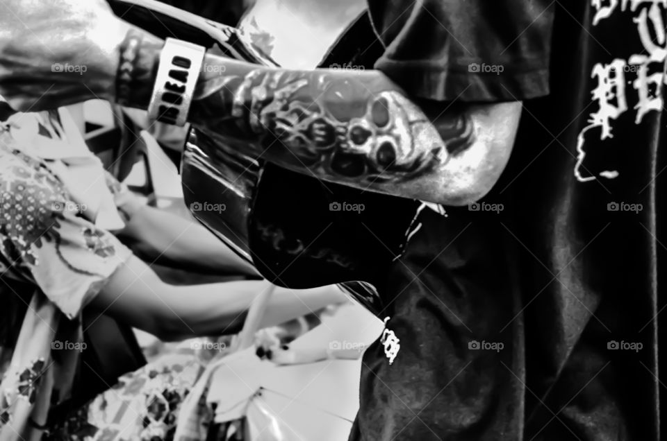 A street singer is playing a guitar on the street, visible with a tattoo on his arm