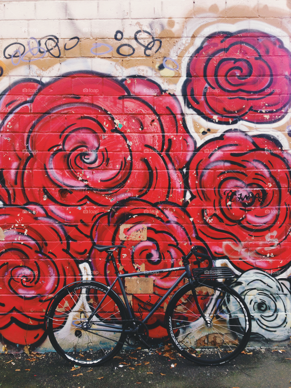 Grayish-black brakeless fixie bicycle standing in front of the wall decorated with bright red colored wallart graffiti with rose flowers