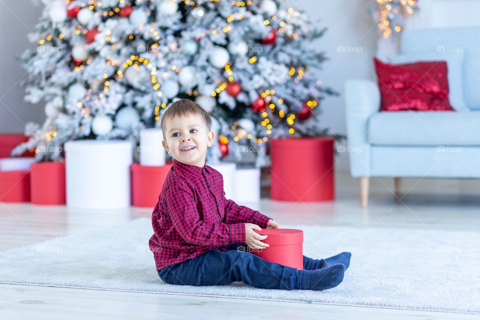 boy and gift box next to christmas tree