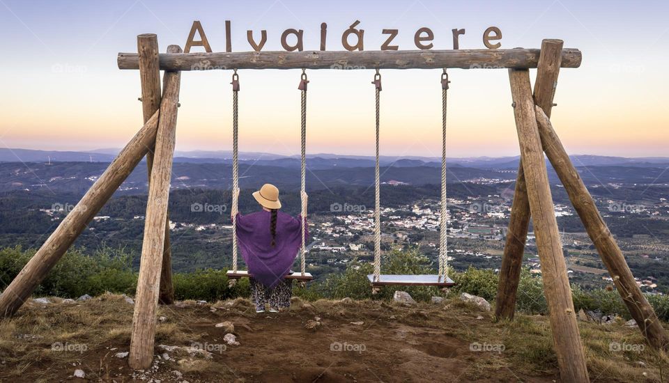 A woman relaxes on a large swing enjoying the landscape around Alvaiazere at sunset 