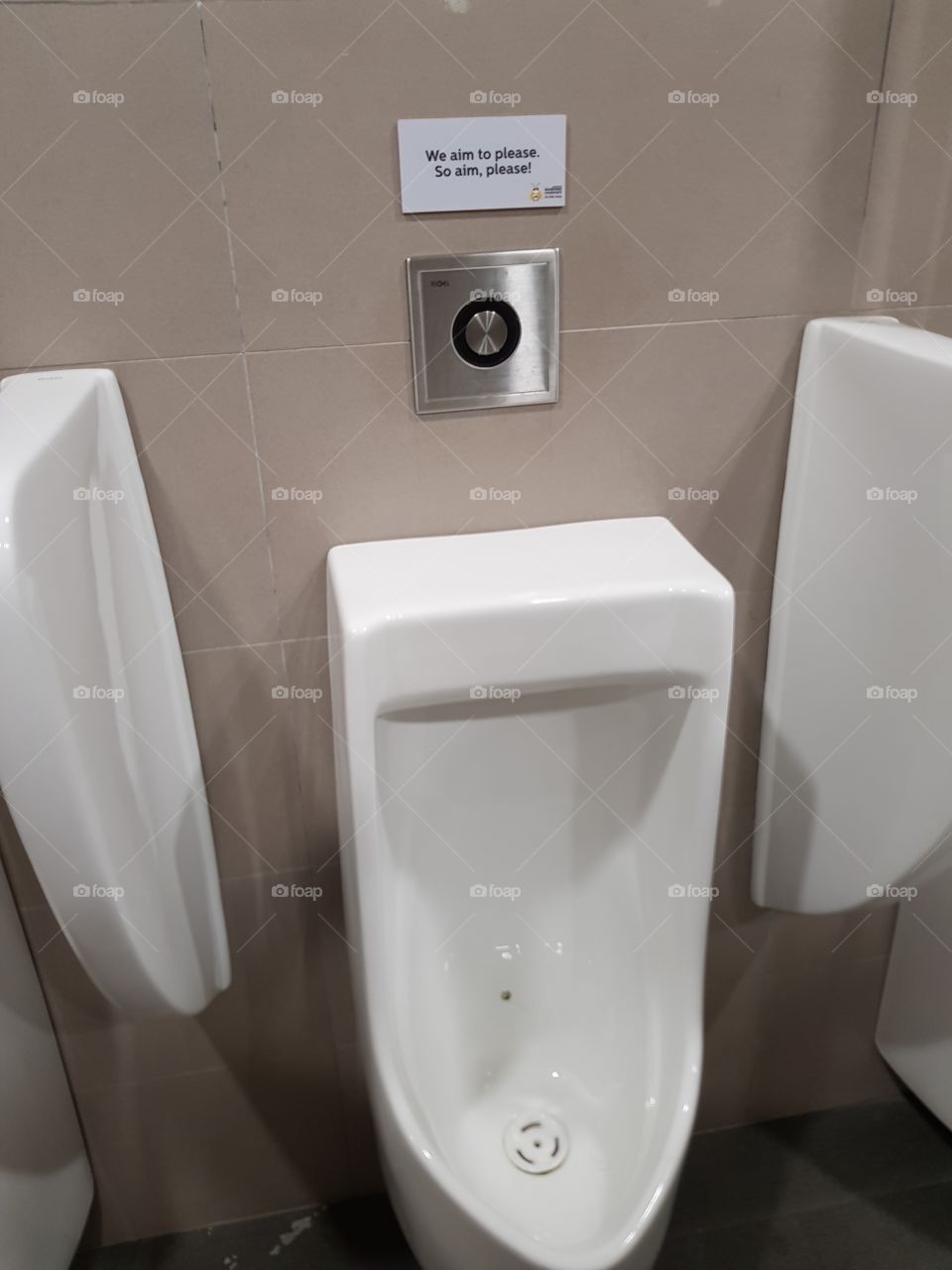 Urinal at a public bathroom with a cheeky sign reminding users to aim