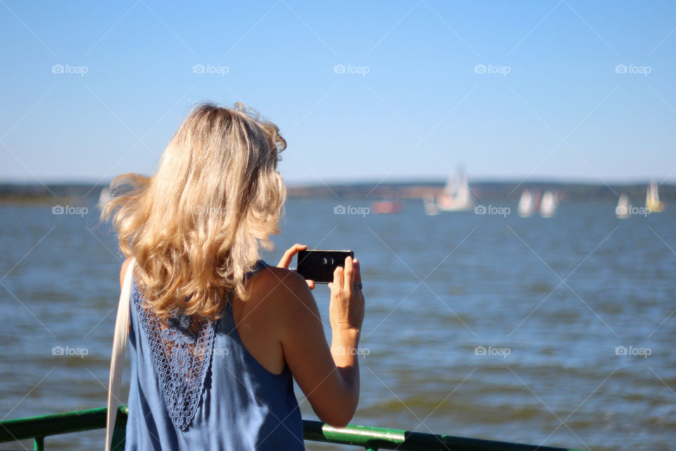 girl with blonde hair pictures of sailboats in the sea by a mobile phone