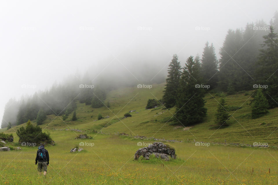 Man hiking on the meadow in foggy mountain 