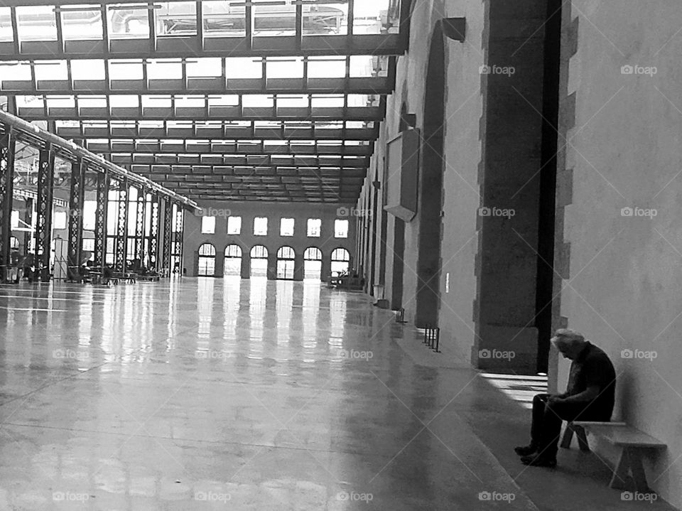 A lonely man sitting on a bench in a huge place. Loneliness, waiting or rest ? 
Former industrial site renovated and rehabilitated into a multicultural place "les ateliers des Capucins" in Brest, Brittany, France.