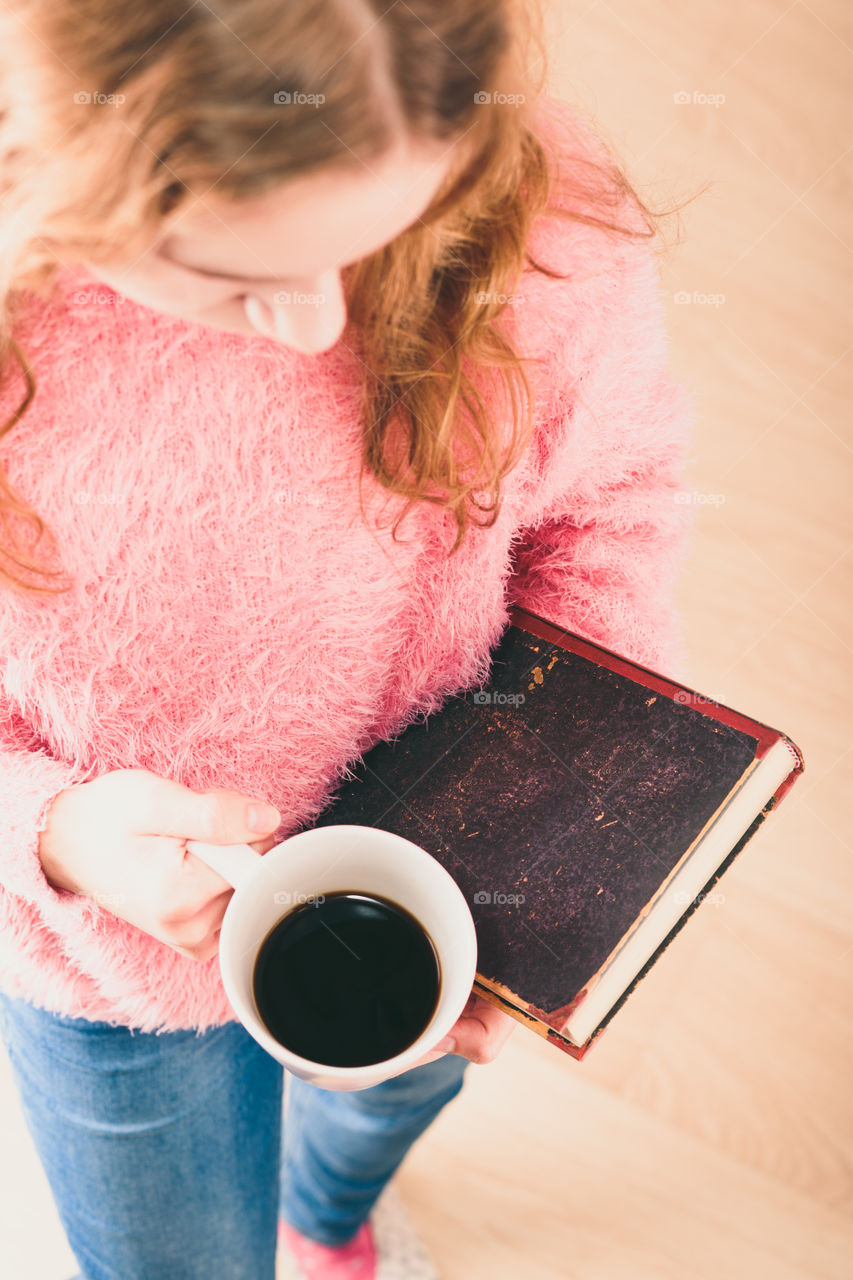 Enjoying the reading a book. Young girl holding book and cup of coffee going to relax with book. View from top