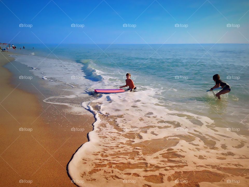 A young boy and girl hopping through the waves on their boogie boards on a bright summer day.