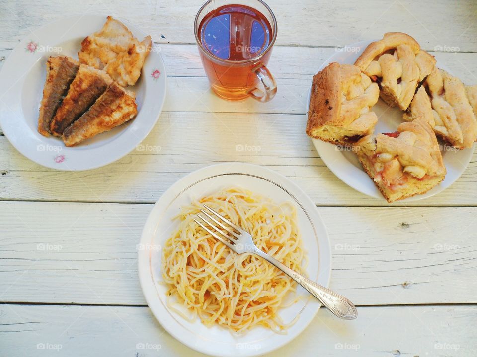 noodles in a dish, homemade cake, fried fish and a cup of tea on the table