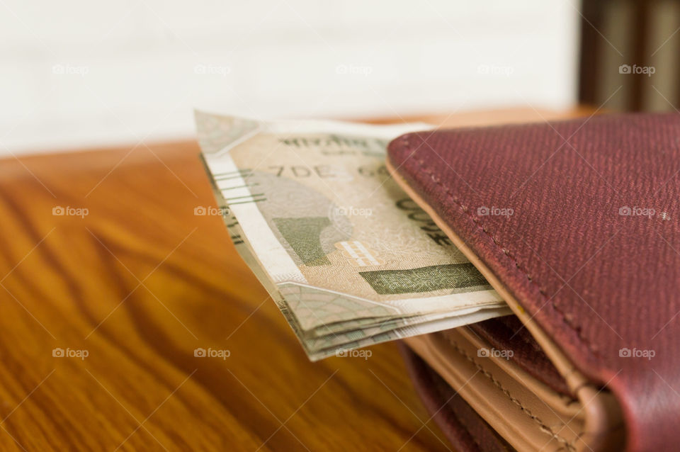 Indian five hundred (500) rupee cash note in brown color wallet leather purse on a wooden table. Business finance economy concept. Side angel view, extreme close up with copy space room for text.