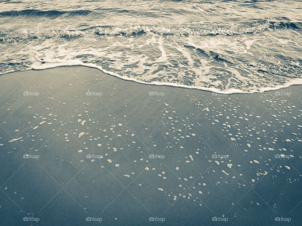 Texture and background of soft wave foam on sandy beach in green tone sepia