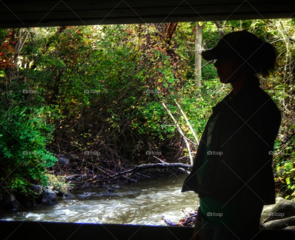 silhouette of woman standing under a bridge by a river