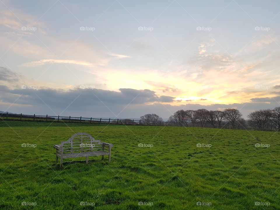Empty bench waiting for a couple to come watch the sun rise and set across the grassy field