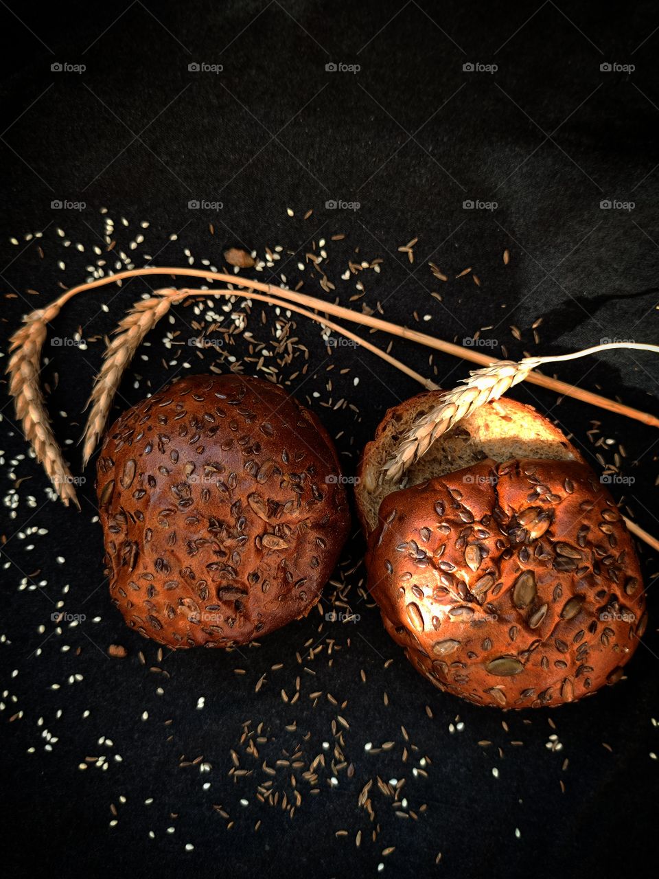 bread rolls coated with grain, caraway seeds and sunflower seeds. ears of wheat. caraway. Black background. a ray of light