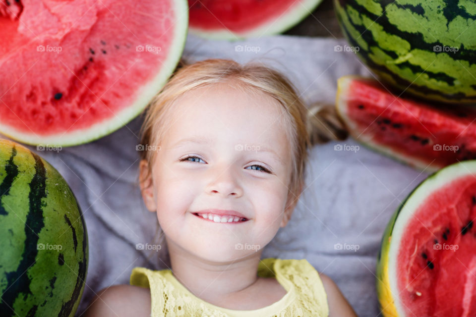 Little girl with blonde hair lying on the blanket with fresh watermelon 