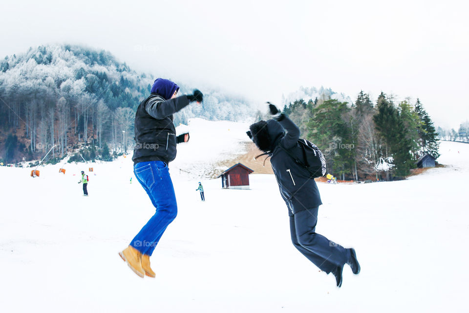 Man and woman jumping in the snow. Mountain ski track covered with snow. Happy moments.