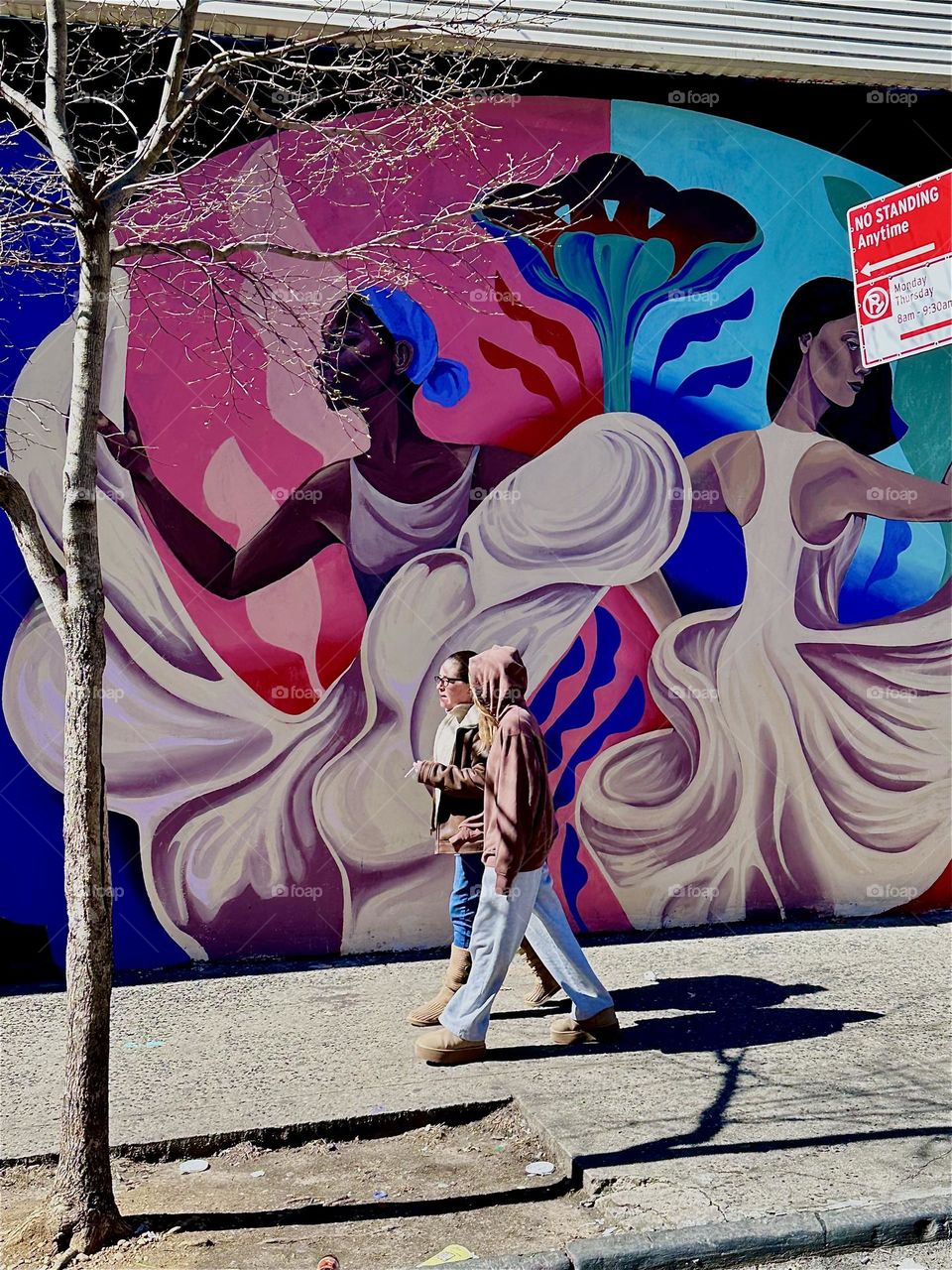 This is one part of a beautiful art mural on „Jefferson Street“ off „Broadway“ in „Bushwick“, Brooklyn showing a dancing African lady in a long flowing white dress and pedestrians passing by on the sidewalk. 2024. Hypnotic Productions