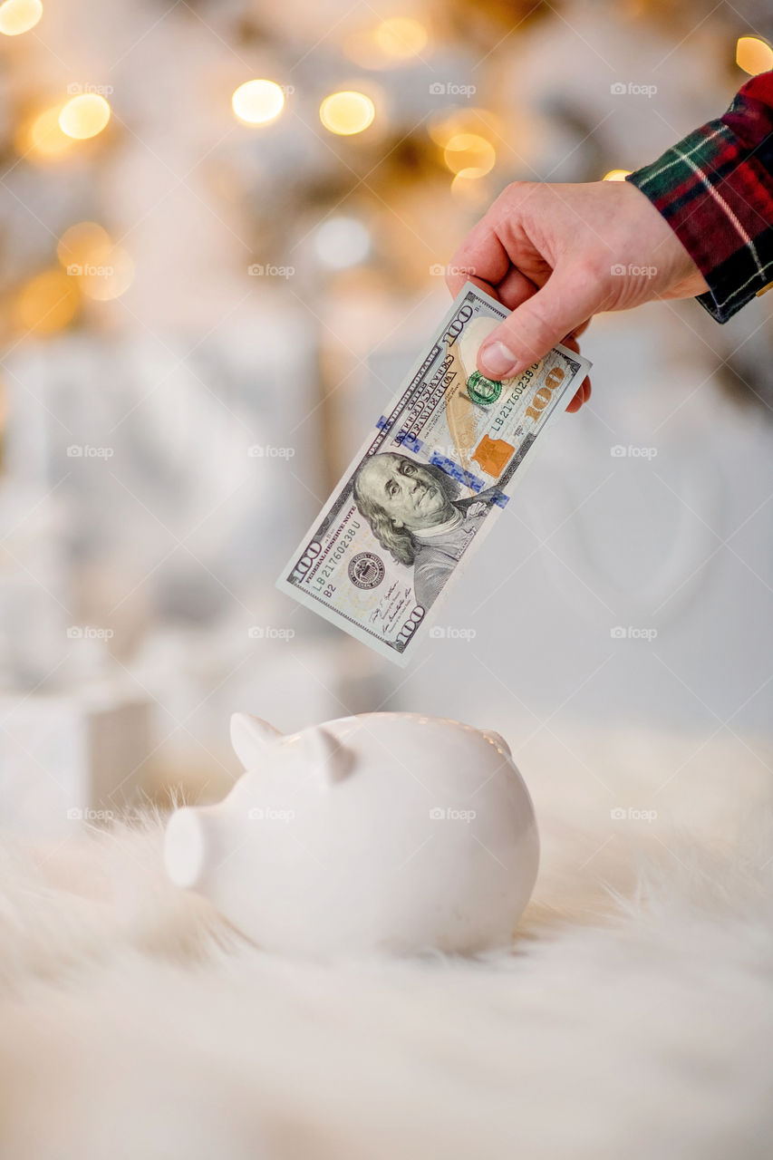 piggy bank with 100 dollars banknote in festive New Year atmosphere of scenery.  Magical bokeh with Christmas tree and bright lights.