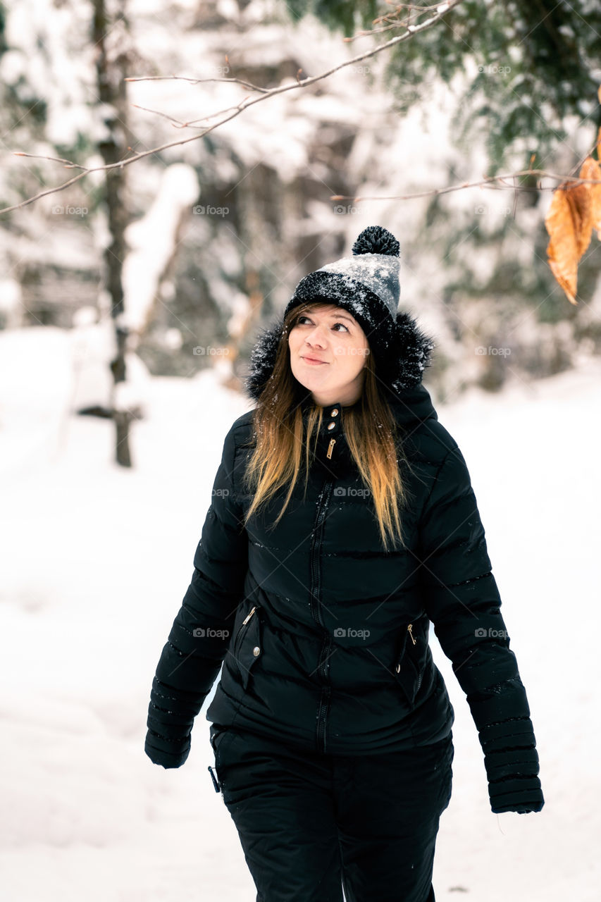 Young attractive female standing outside looking away at a snow covered winter wonderland scene. 