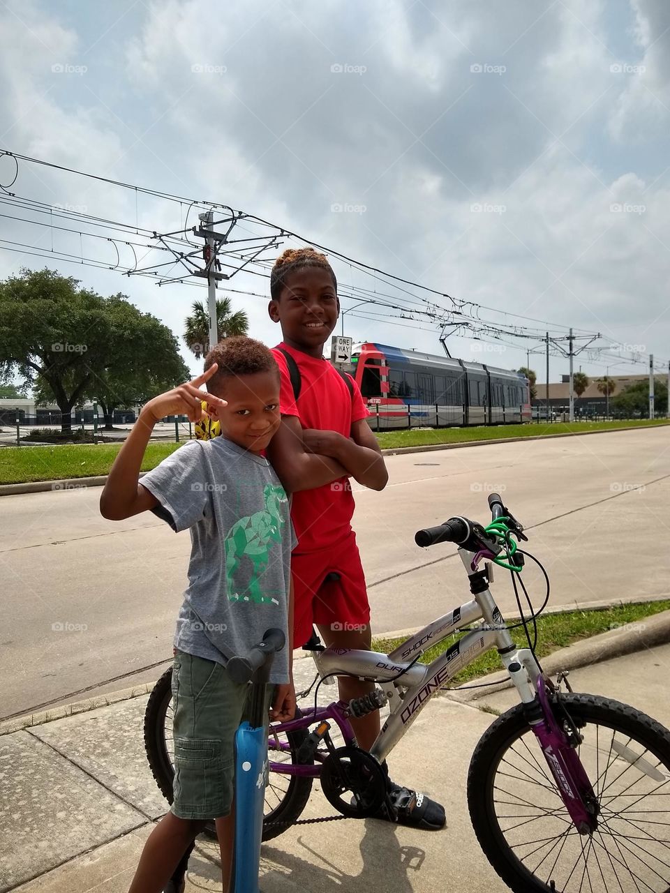 Two boys on the way to the park on a cloudy Spring day. One on a bike 🚲, the other on a scooter 🛴.
