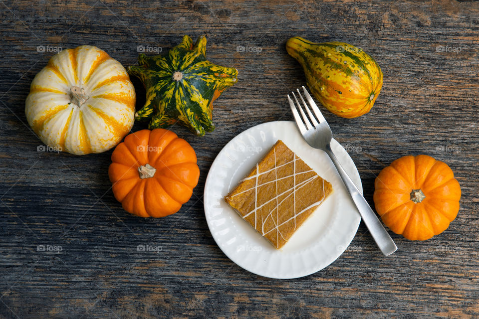 Looking down on a wooden table with a white dish of pumpkin cheesecake surrounded by colorful gourds.