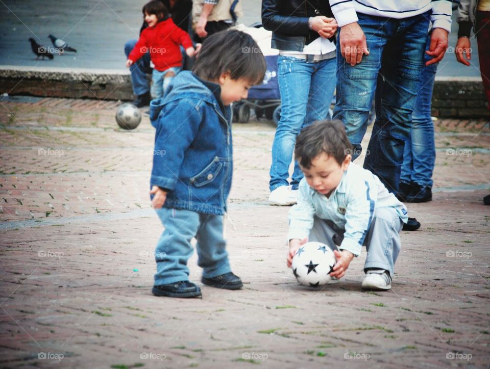 Can I play?. Two toddlers play with the soccer ball in the street