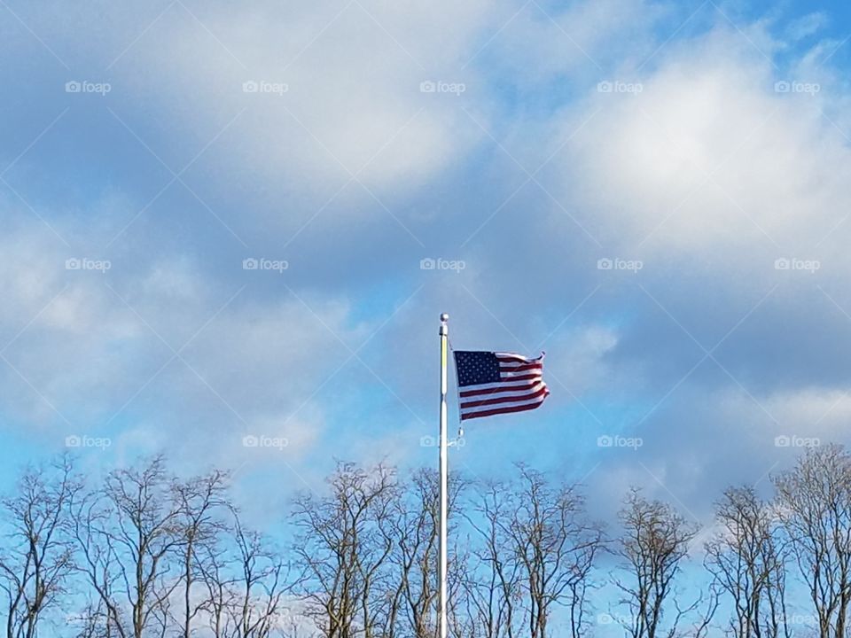 American flag blowing in the wind on a cloudy blue sky day