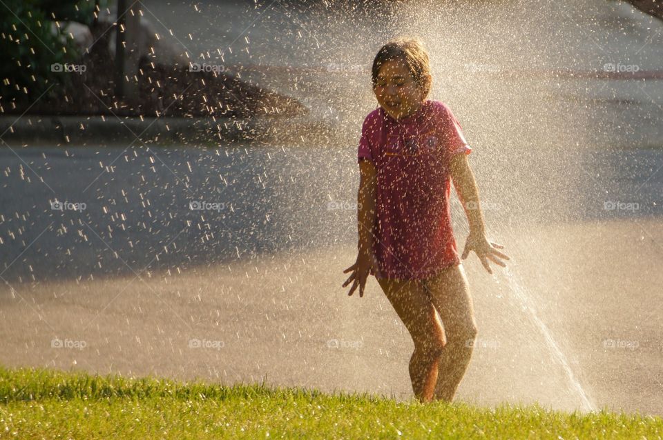 Girl playing in a Sprinkler in the yard in the summer 