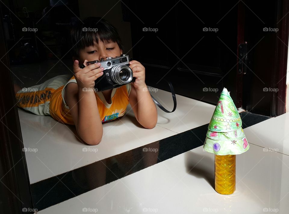 young boy taking picture of his paper diy mini christmas tree with analog vintage film camera
