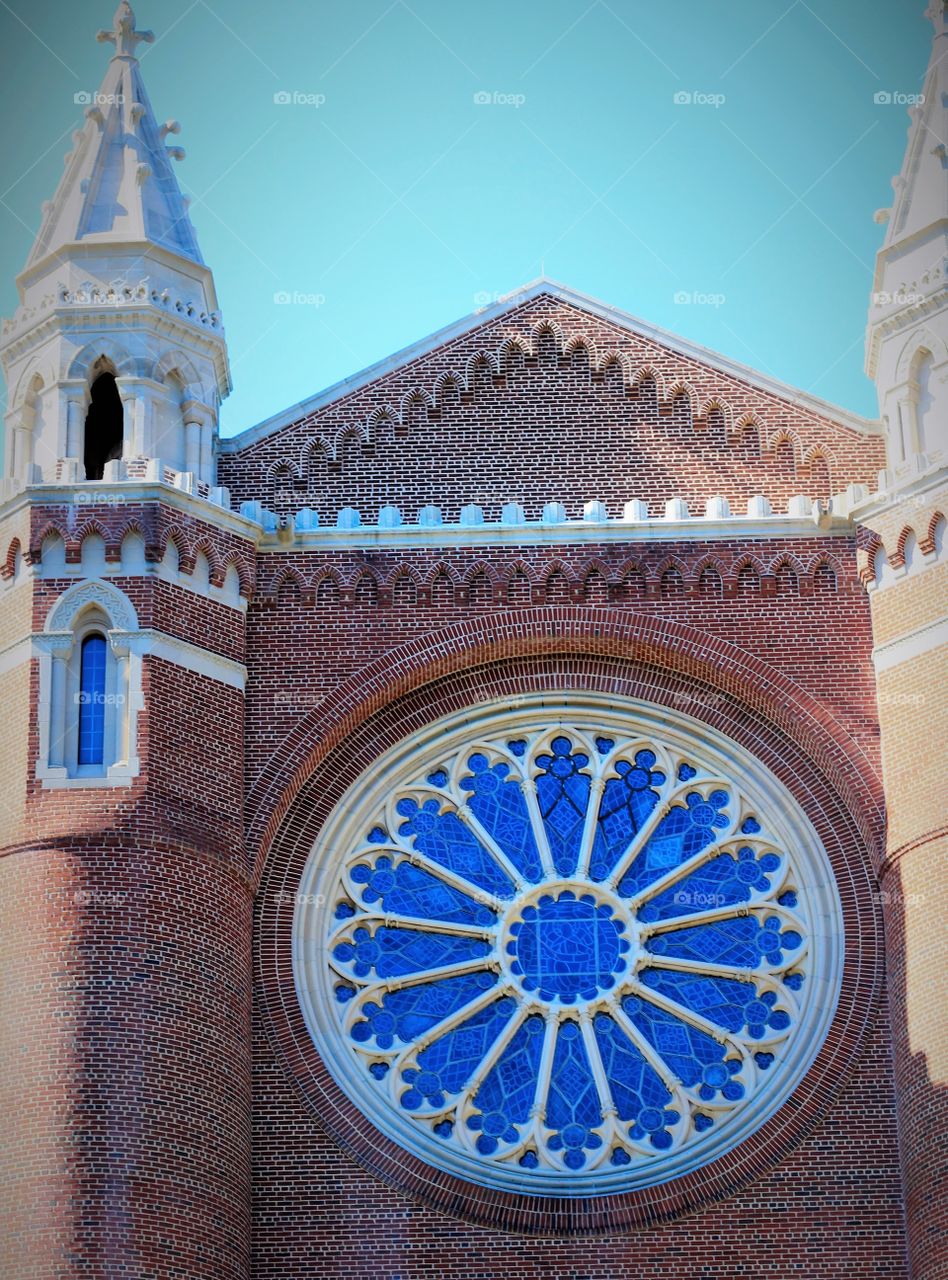Church steeple and mosaic round window  and red brick against nice blue sky.