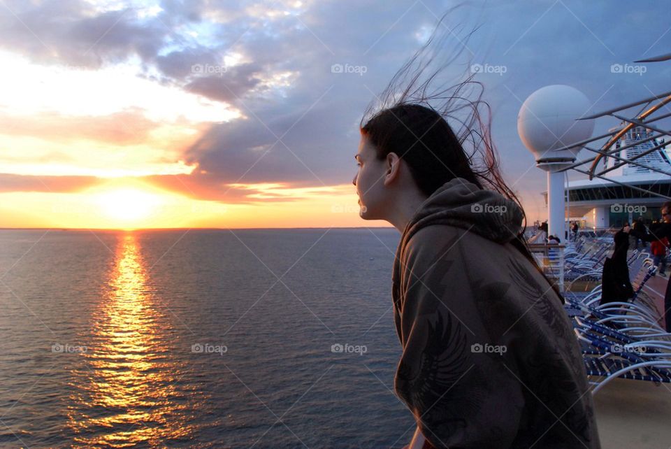Young girl looks over a boat at sunset