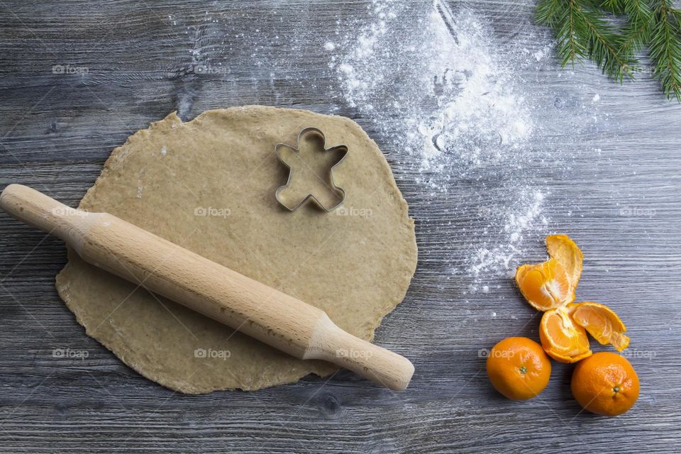 Cooking Christmas gingerbread cookies on a wooden table with tangerines and green Christmas trees.