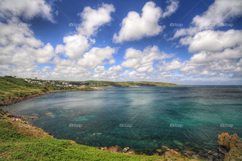 A beautiful Cornwall coastal scene of an expansive bay with green sea and blue sky with white fluffy clouds.