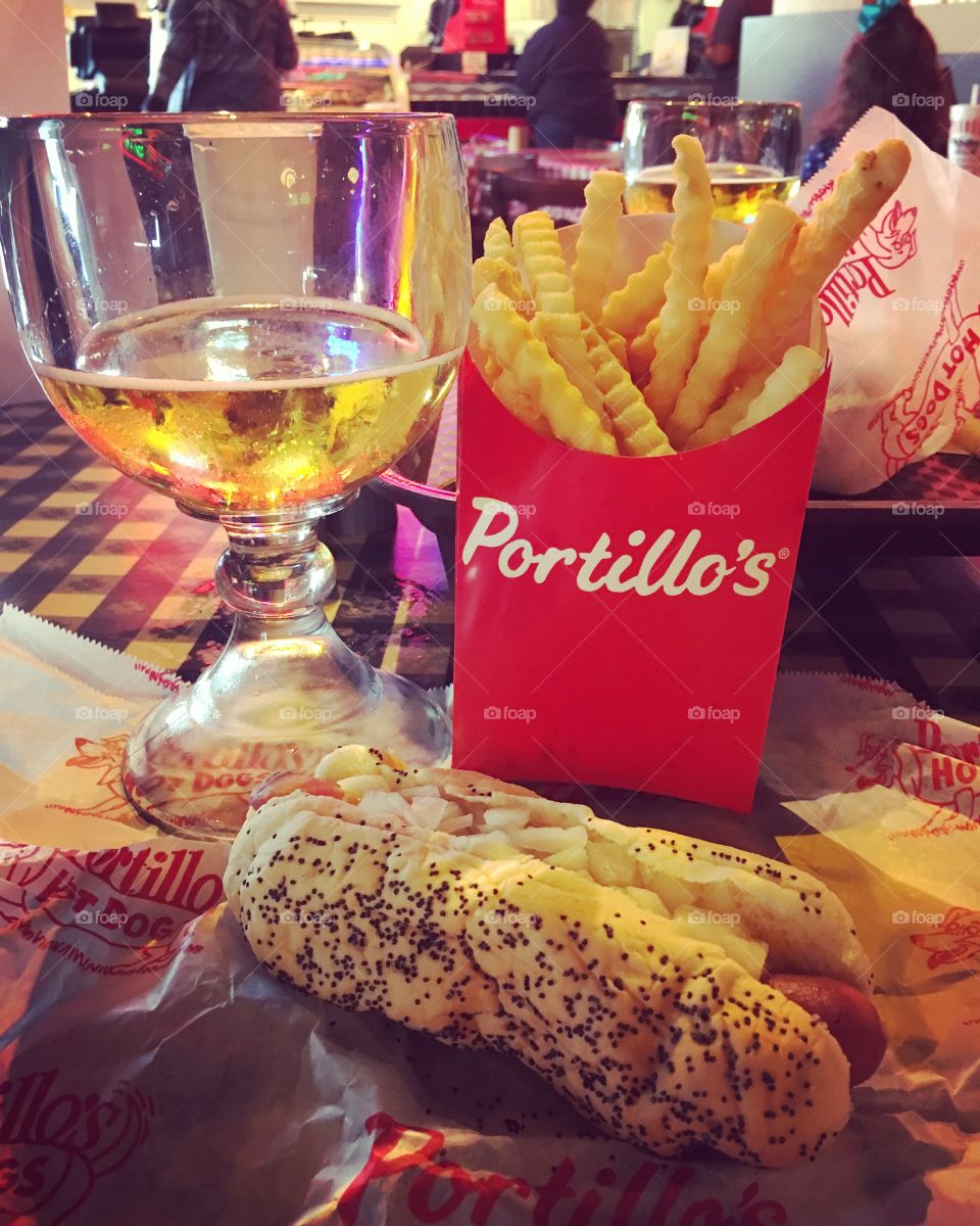 Hot dog with mustard and onions on a bun with fries and a beer. 