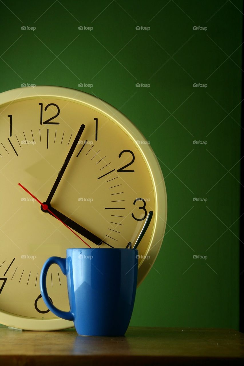 blue coffee mug with teaspoon and an analog clock