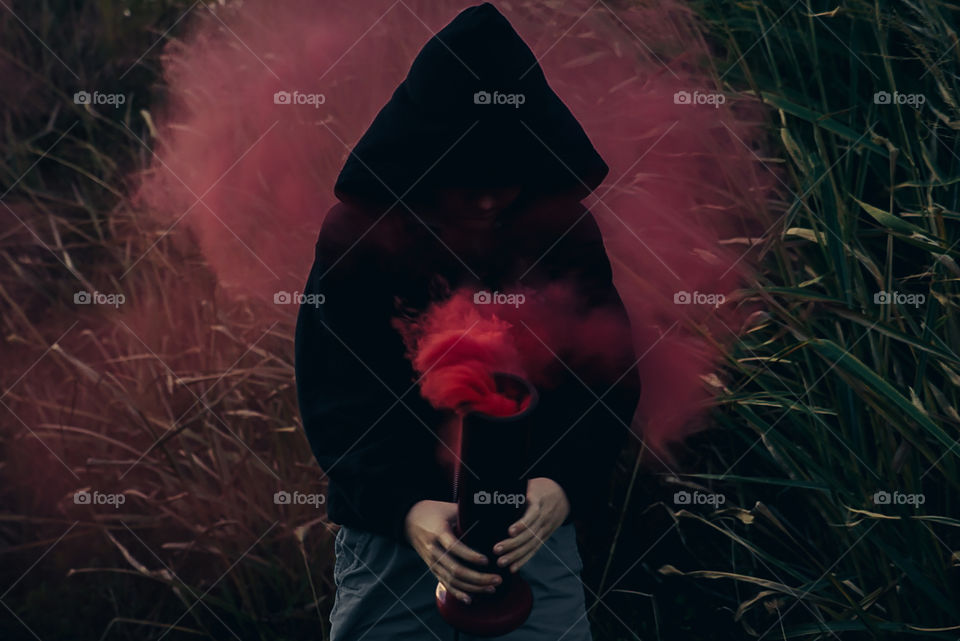 Ominous hooded black figure hold antique beaker that has an explosion of red smoke bellowing out of it 