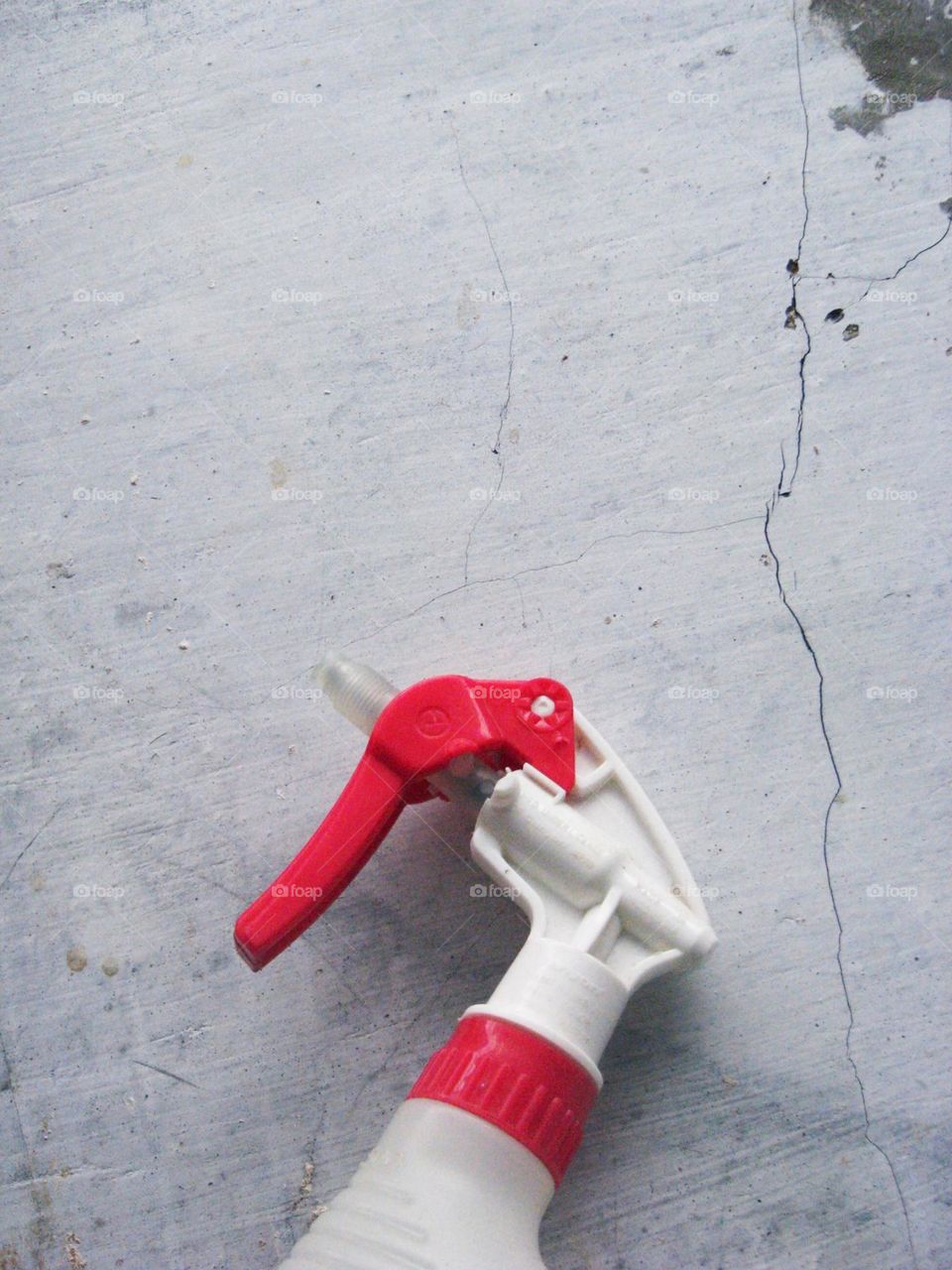 Close-up of a spray bottle with red and white spray heads lying on a rough gray surface