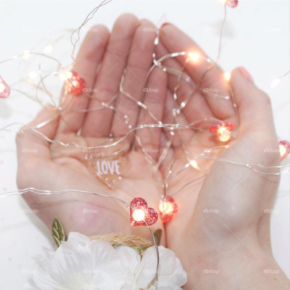 Hands cupping a string of heart lights and a live heart! White flowers adorn the one wrist! I give you my love and my heart!