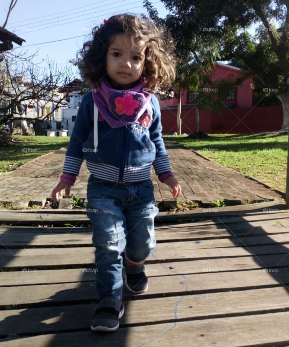 Menina de 2 anos vestida com calça jeans. Caminha sobre uma Ponte.