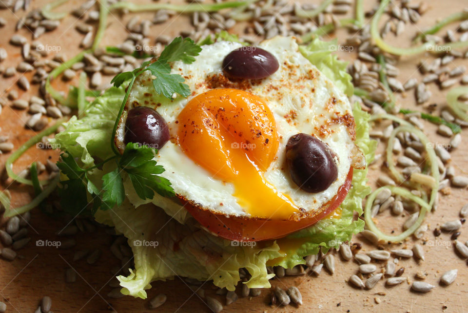 Tasty burger with fried egg, olives, lettuce, seeds, yolk...