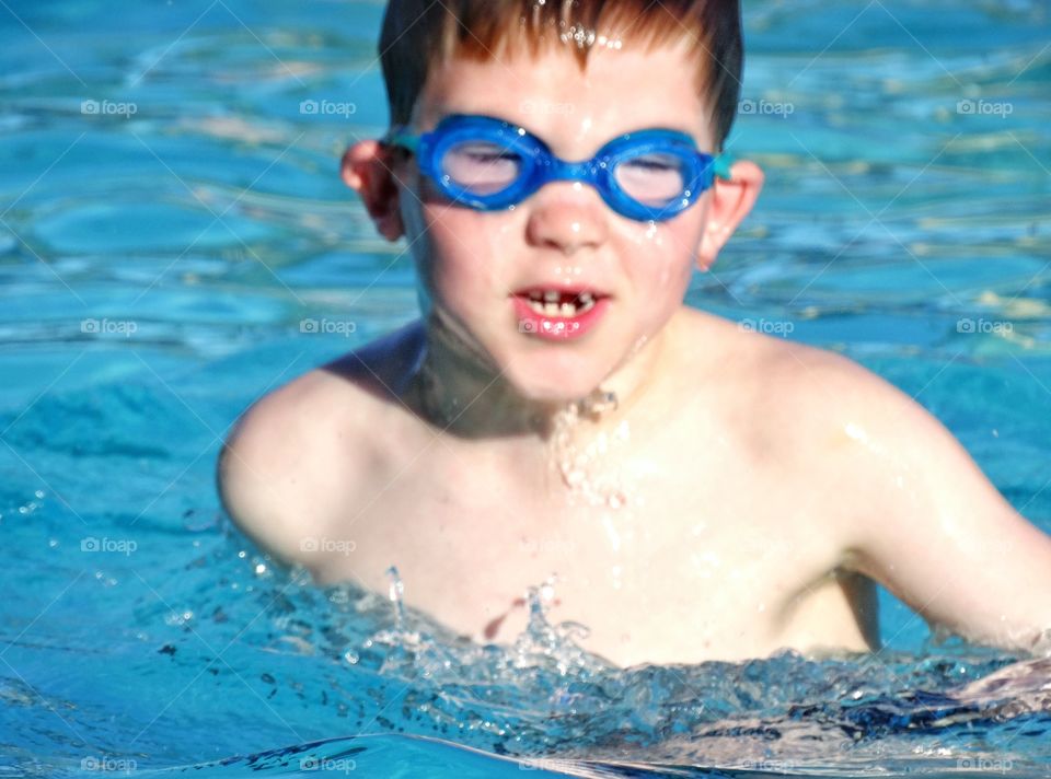 Happy Young Swimmer. Young Boy Splashing In Blue Water
