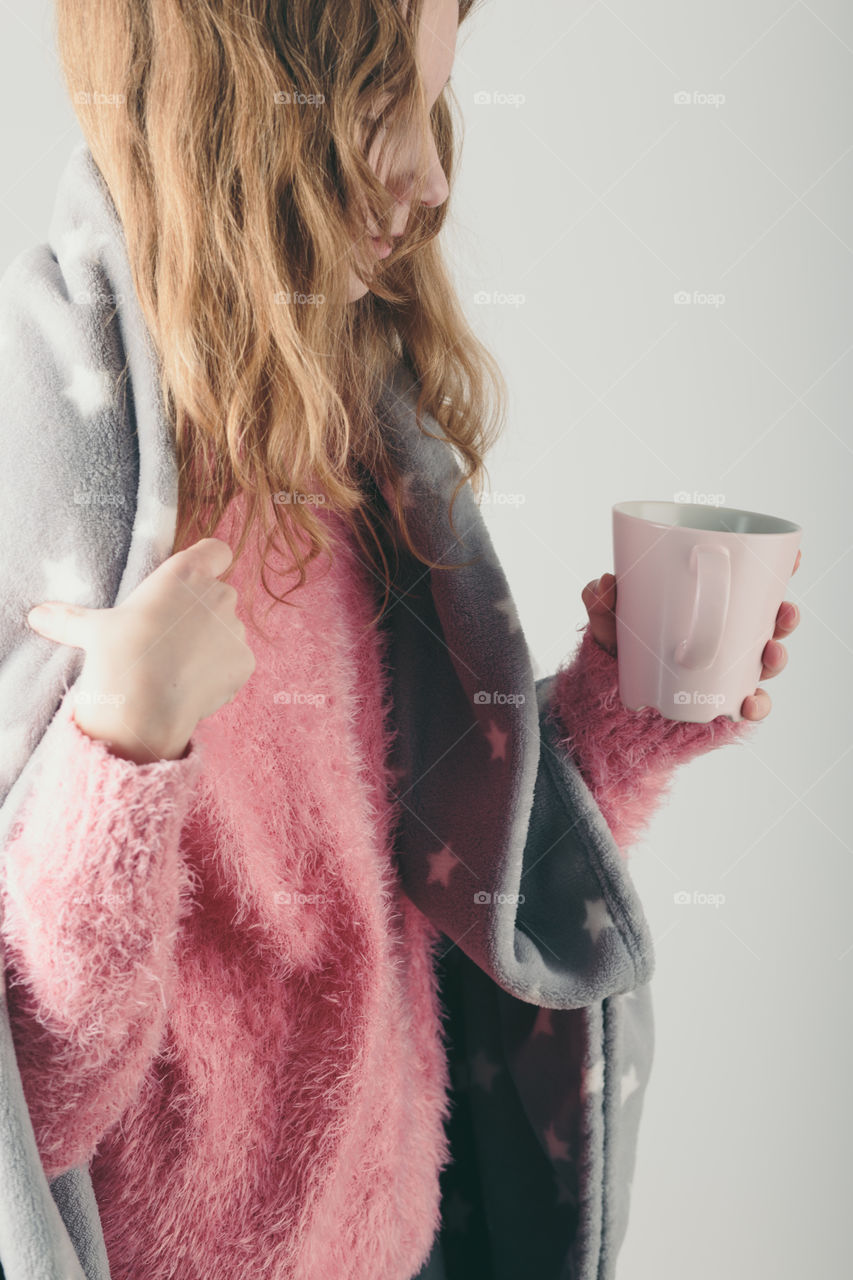 Young woman has caught cold, has day off, sick day, wrapped in blanket, holds cup of herbal tea. Profile portrait view