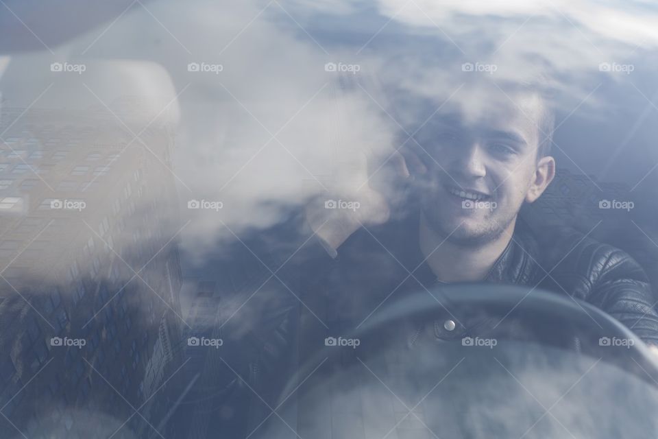 young man in his car at the wheel talking on a mobile phone 