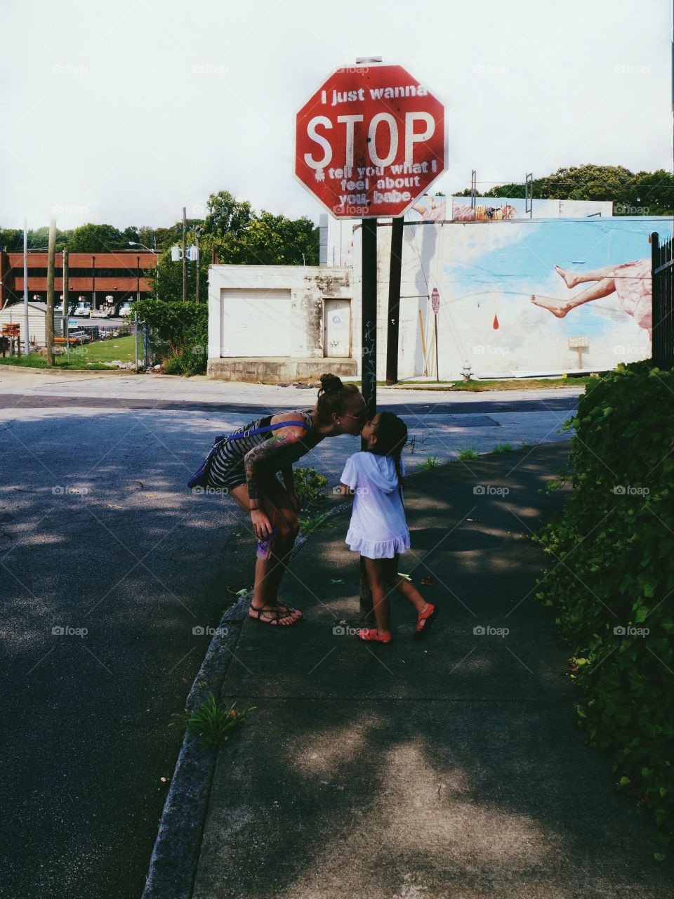 Mother kissing her daughter near sign board on street