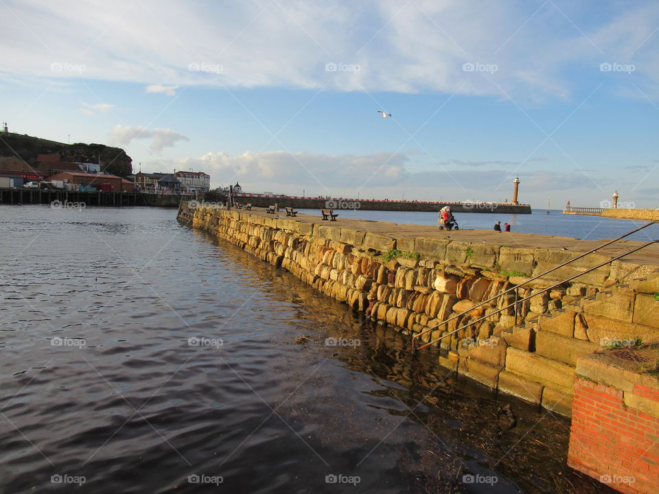 Whitby harbour with the sun shining down on the pier stone wall