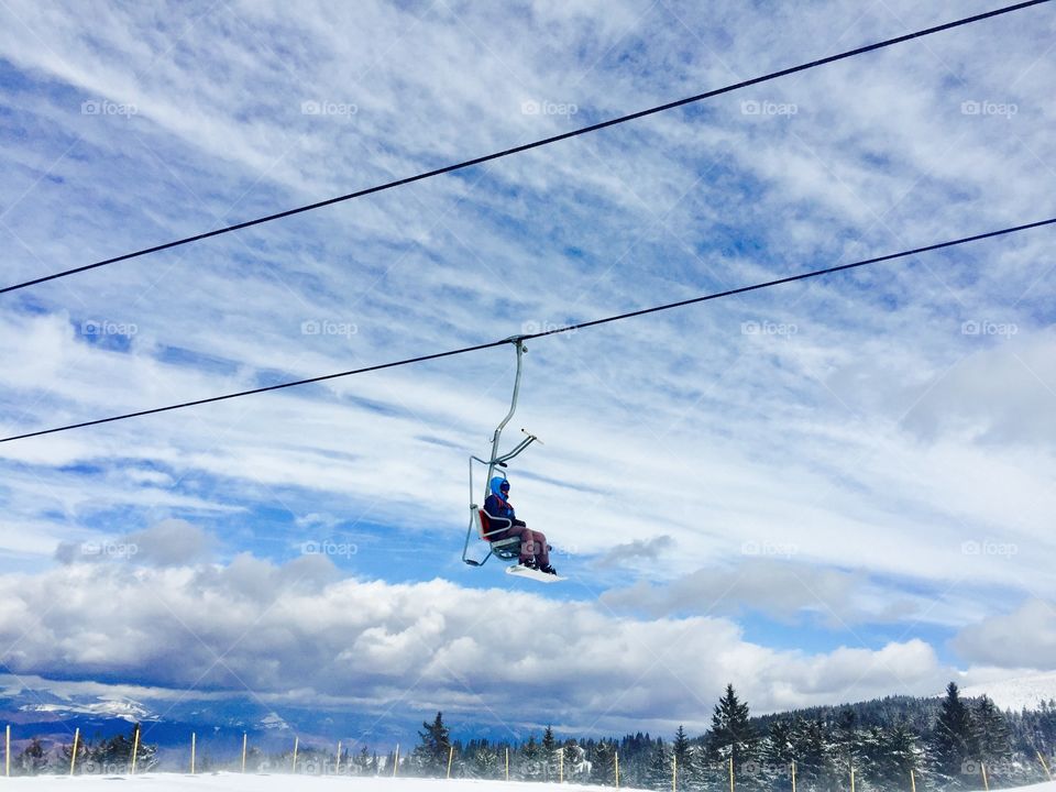 Single skier in the ski lift over forest of evergreen trees on a day with blue sky 