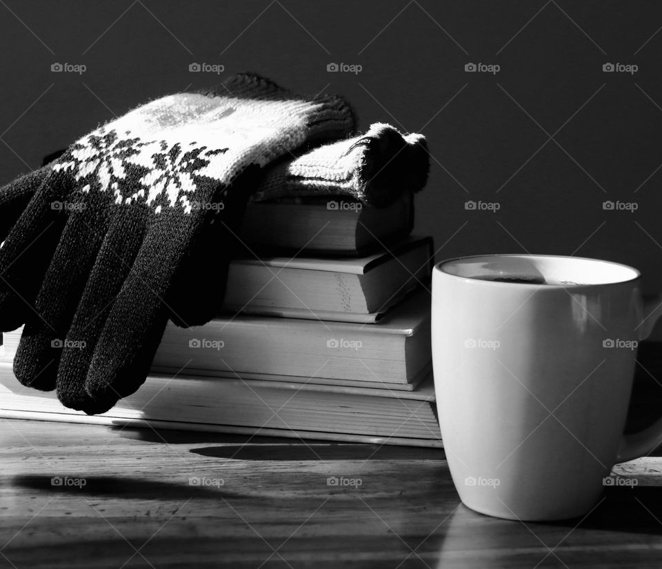Gloves sitting on a stack of books beside a cup of hot chocolate 
