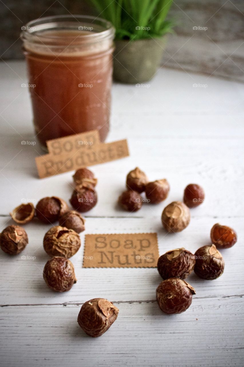 Closeup of soap nuts or soap berries with label and liquid soap for DIY soap products on white wooden surface in natural light