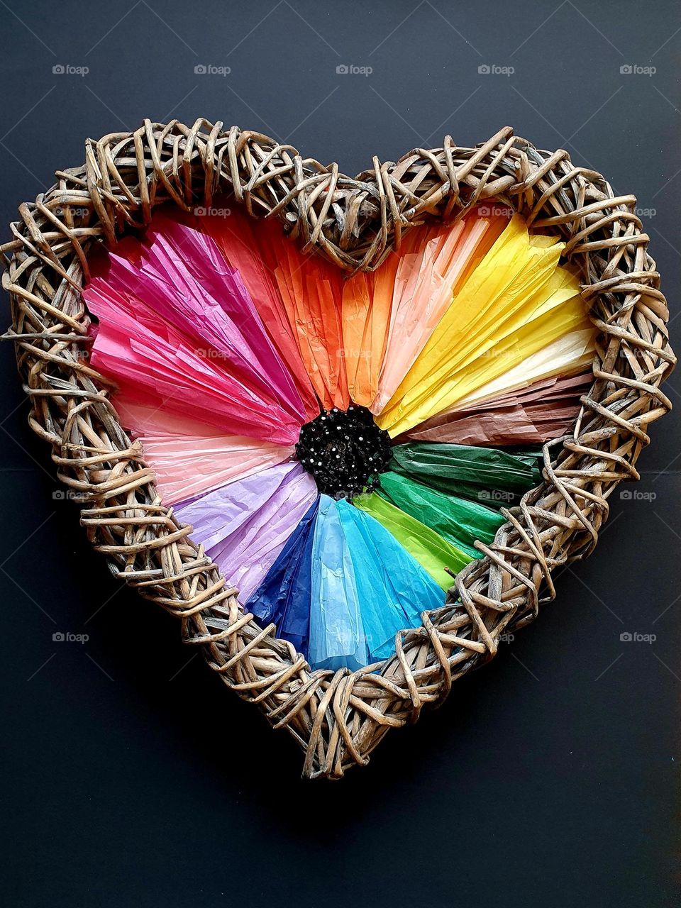 Flatlay composition of a heart-shaped flower made of multi-coloured silk papers, black beads and heart-shaped wicker wreath, creating a colour explosion