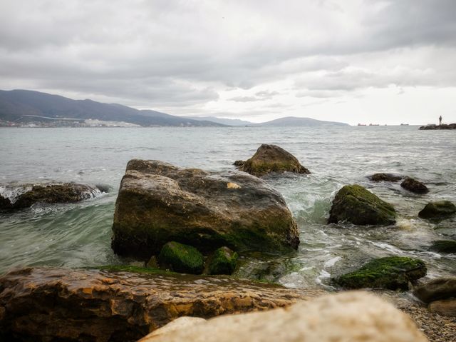 Stones overgrown with algae. It's raining. The waves of the sea. Mountain range.
