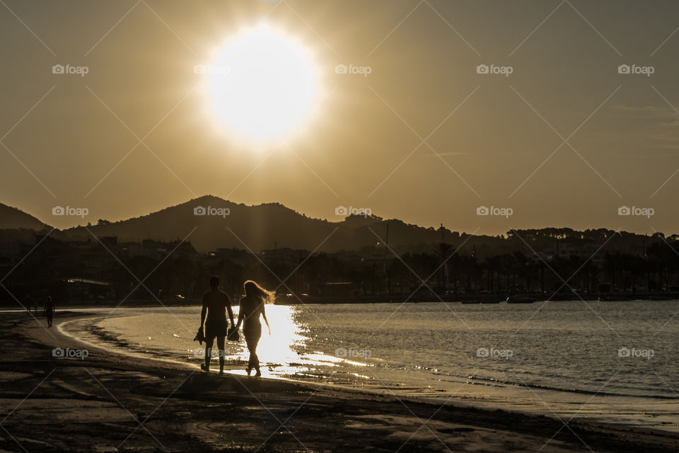 A man and a woman walking on the beach at sunrise 