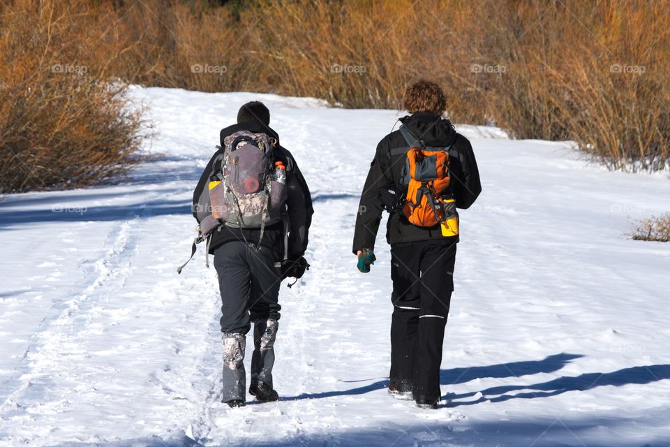 Two men hike side by side along a snowy path.